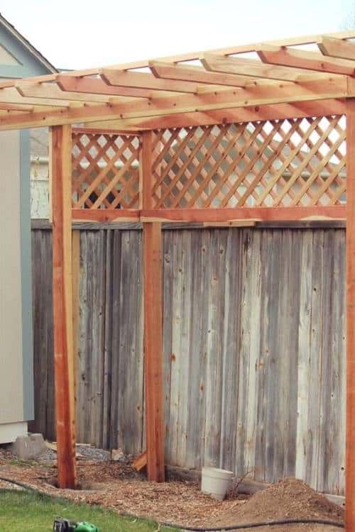 a wooden pergolated area in front of a house with a hose attached to it