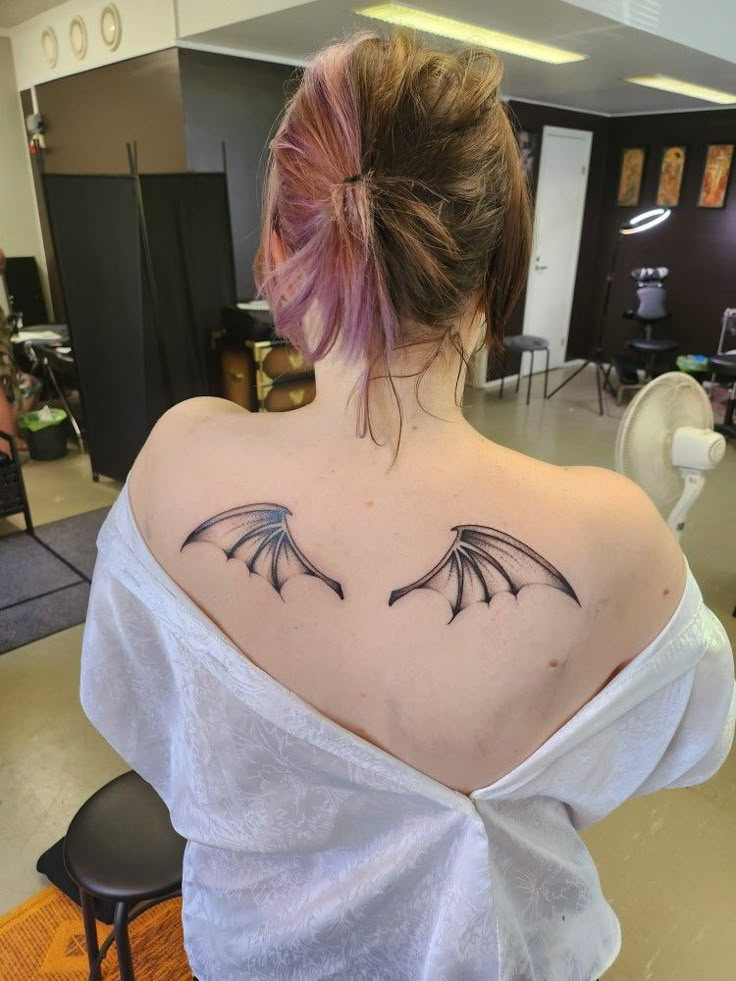 the back of a woman's shoulder with wings tattooed on her left upper arm