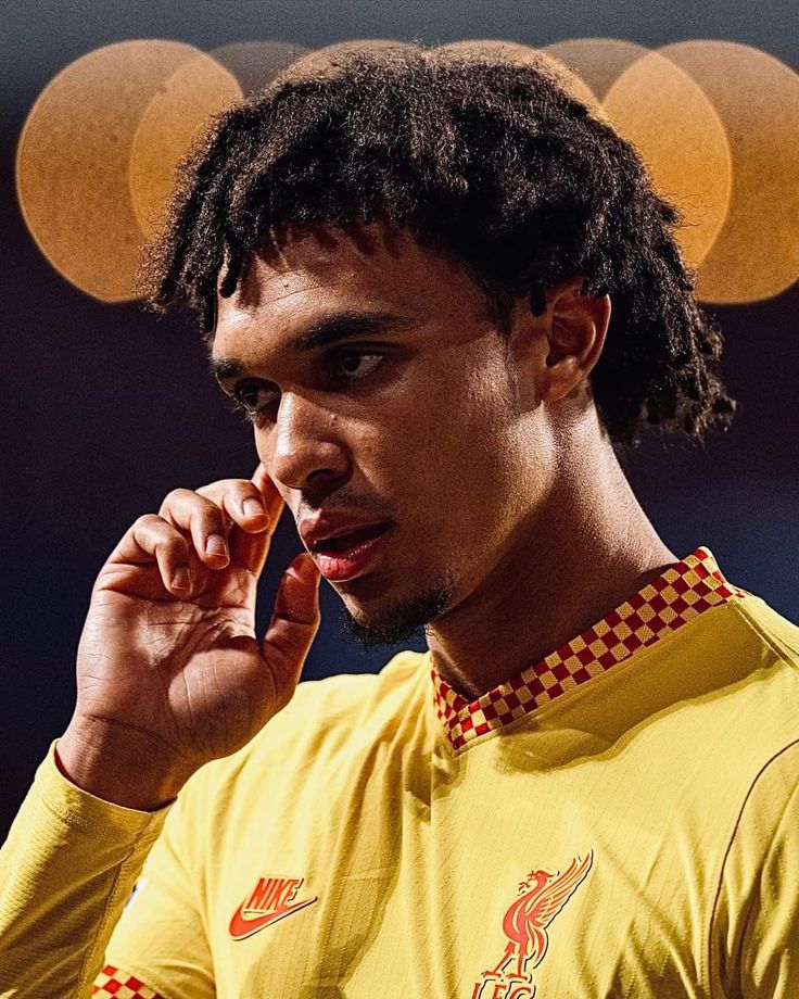 a young man talking on a cell phone while wearing a yellow soccer shirt with checkered trim