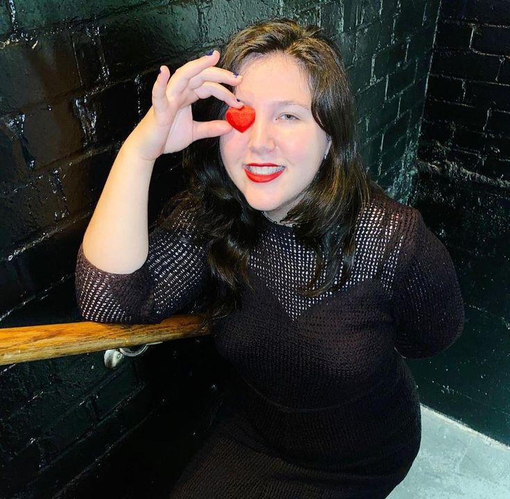 a woman holding a skateboard in front of her face while posing for the camera