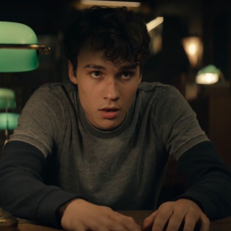 a young man sitting at a table in front of a lamp and looking off into the distance