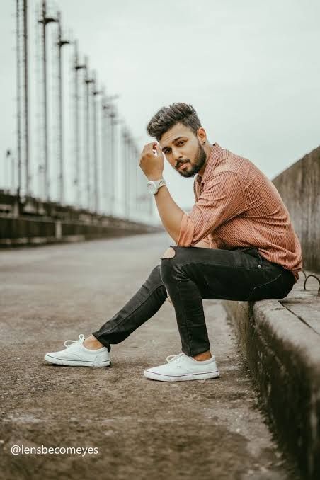 a man sitting on the edge of a cement wall with his hands in his pockets