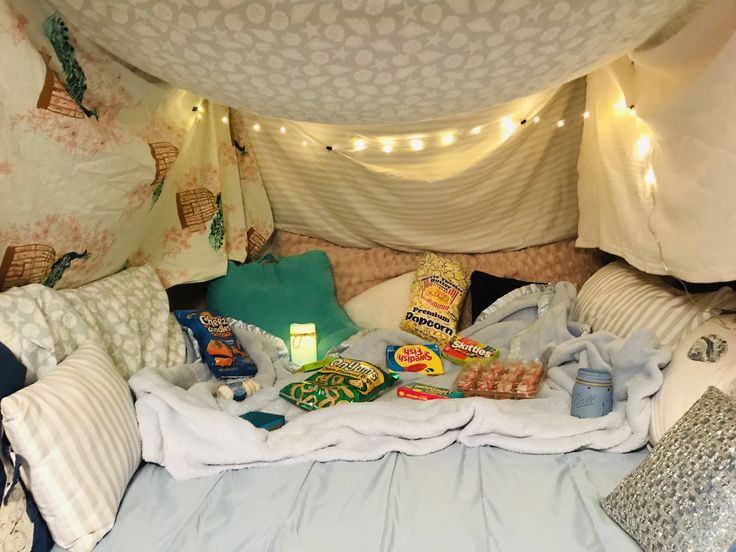 a bed covered in blankets and pillows under a canopy with lights on the ceiling above it