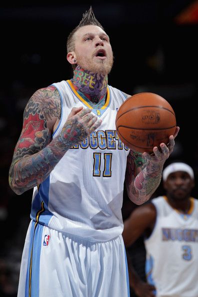 a man with tattoos holding a basketball in his hand and looking up at the ball