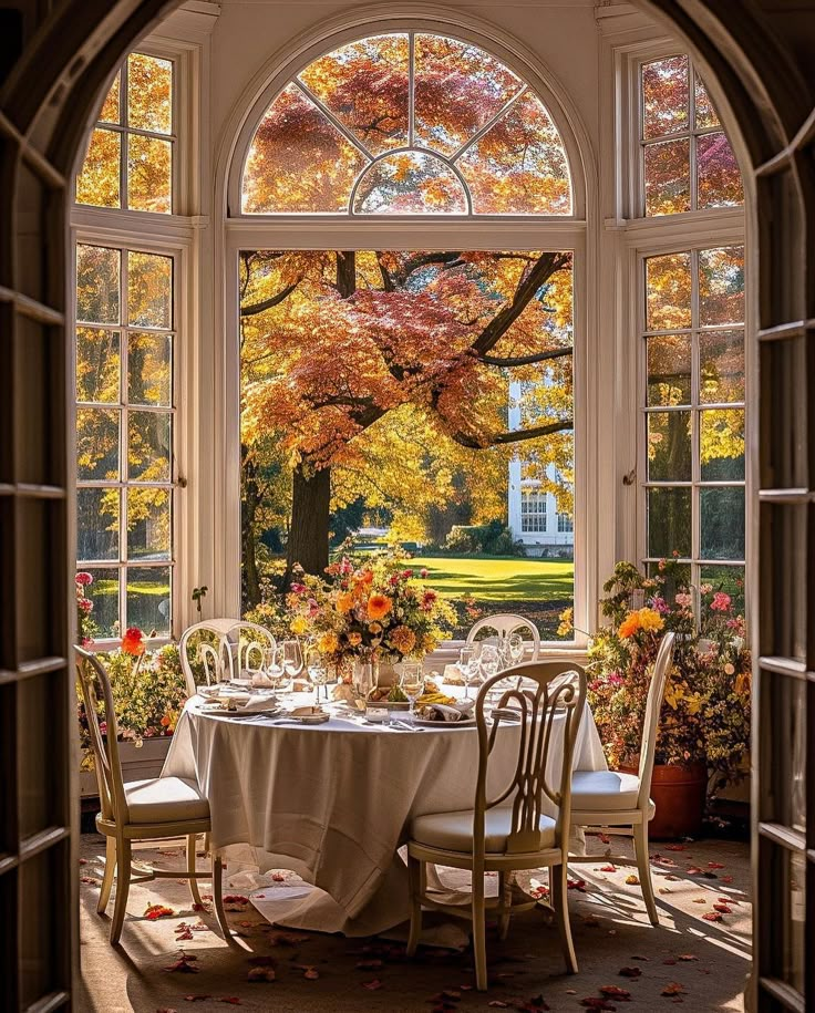 an open window with a table and chairs in front of it, surrounded by fall foliage