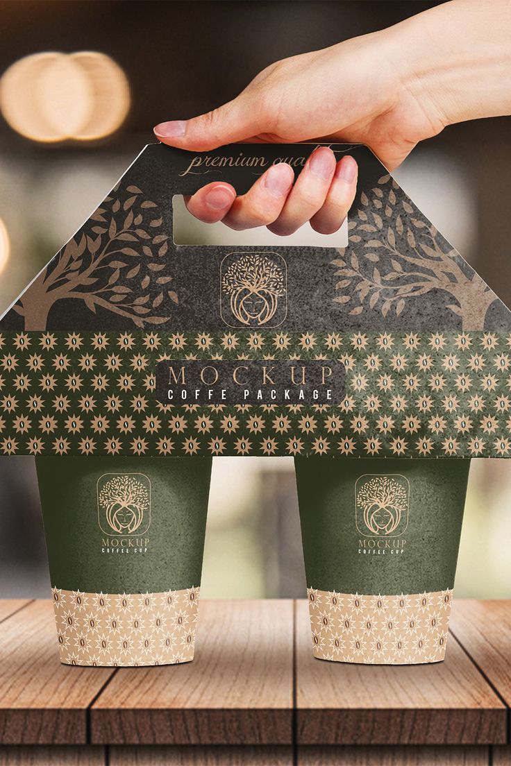 two starbucks coffee cups being held by a person's hand over a wooden table