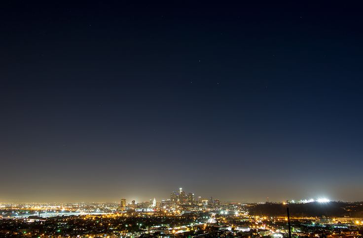 the city lights shine brightly at night from atop a hill in the distance are skyscrapers