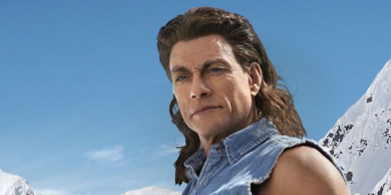 a man with long hair standing in front of snow covered mountains and wearing a denim shirt