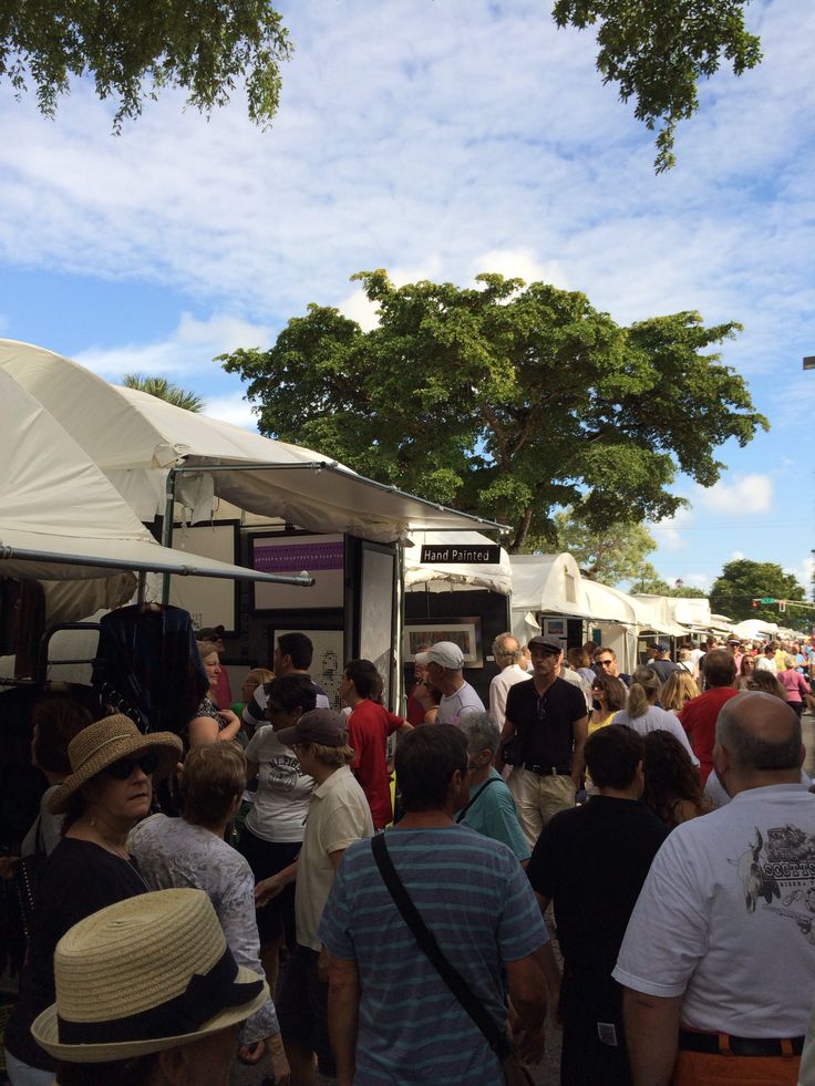 a crowd of people standing around a food truck under a blue sky with white clouds