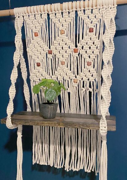 a macrame wall hanging with a potted plant on it and a wooden shelf