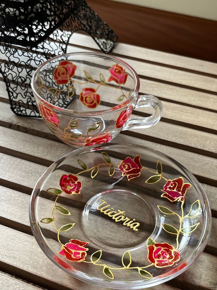 two glass cups sitting on top of a wooden table with flowers painted on the side