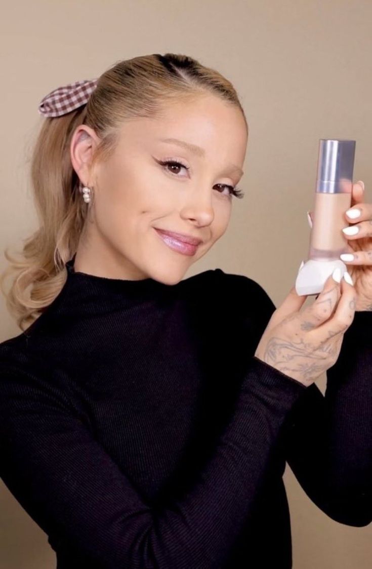 a woman is holding an item in her hand and smiling at the camera while wearing a black top