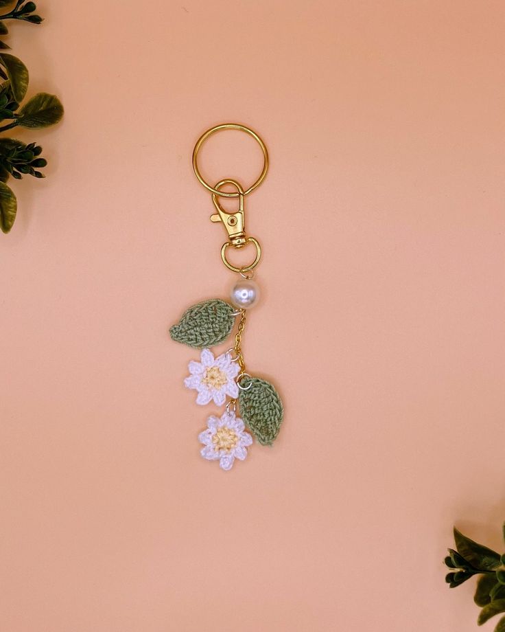 a keychain with flowers and leaves hanging from it's side on a pink surface