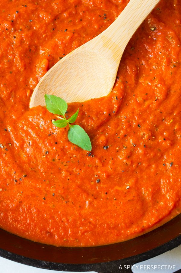 a wooden spoon in a pot of tomato sauce with basil on the side and a sprig of parsley