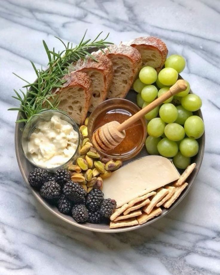 a plate with bread, grapes, crackers and honey on it