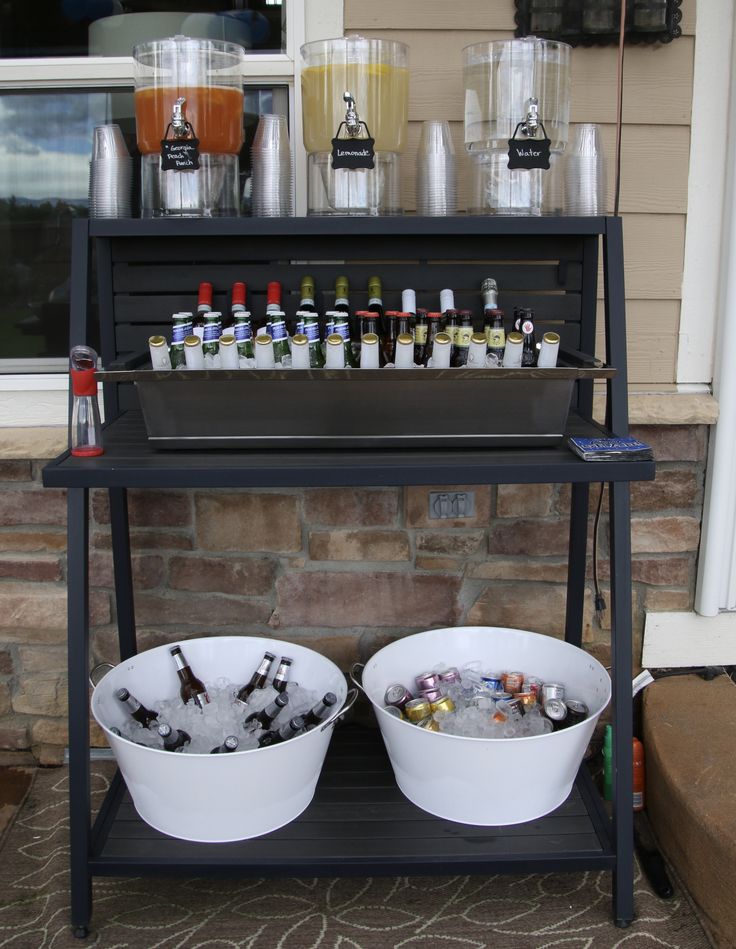 two white buckets filled with drinks sitting on top of a metal shelf next to a brick wall