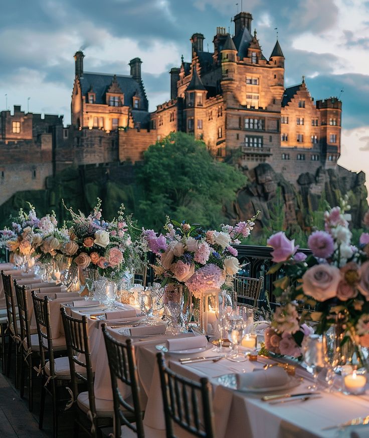 a long table is set with flowers and candles in front of a castle like building