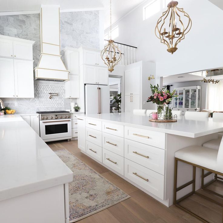 a large kitchen with white cabinets and counter tops, chandelier hanging from the ceiling