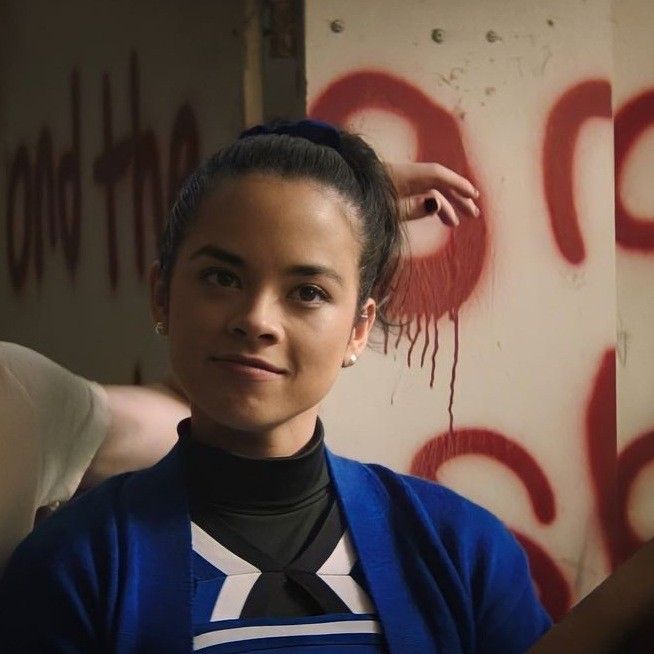 a woman in a blue shirt and black tie standing next to a wall with graffiti on it