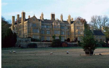 an old building with sheep grazing in the foreground and trees on the far side