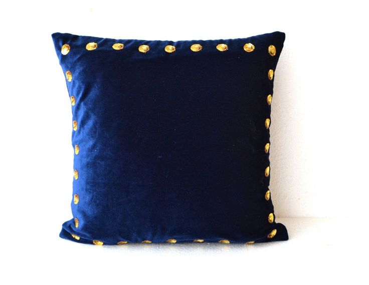 a blue pillow with gold studding on the front and back, sitting against a white wall