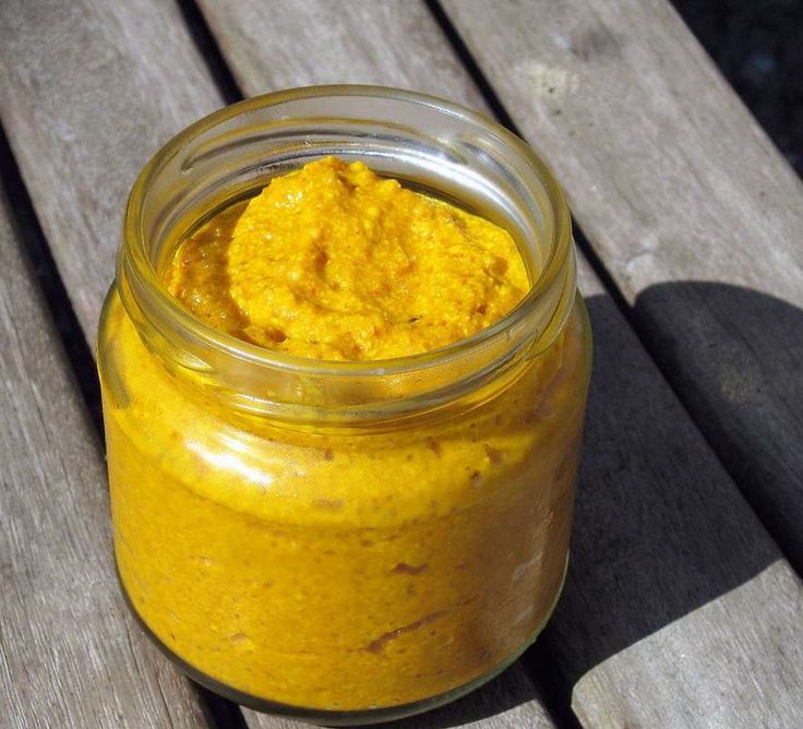 a jar filled with yellow colored food sitting on top of a wooden table next to a bench