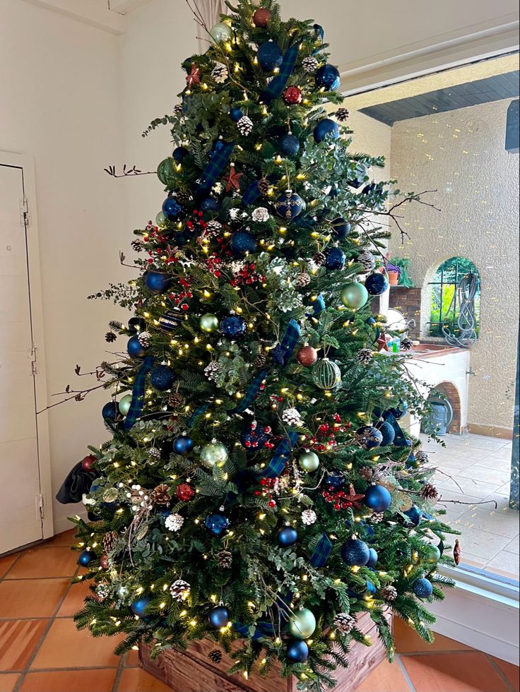 a christmas tree with blue and red ornaments in a potted planter on the floor