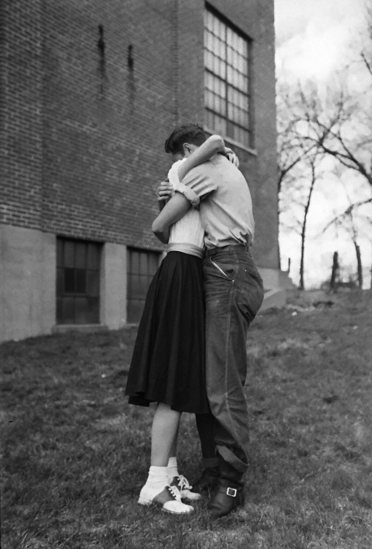 a man and woman embracing in front of a brick building with grass on the ground