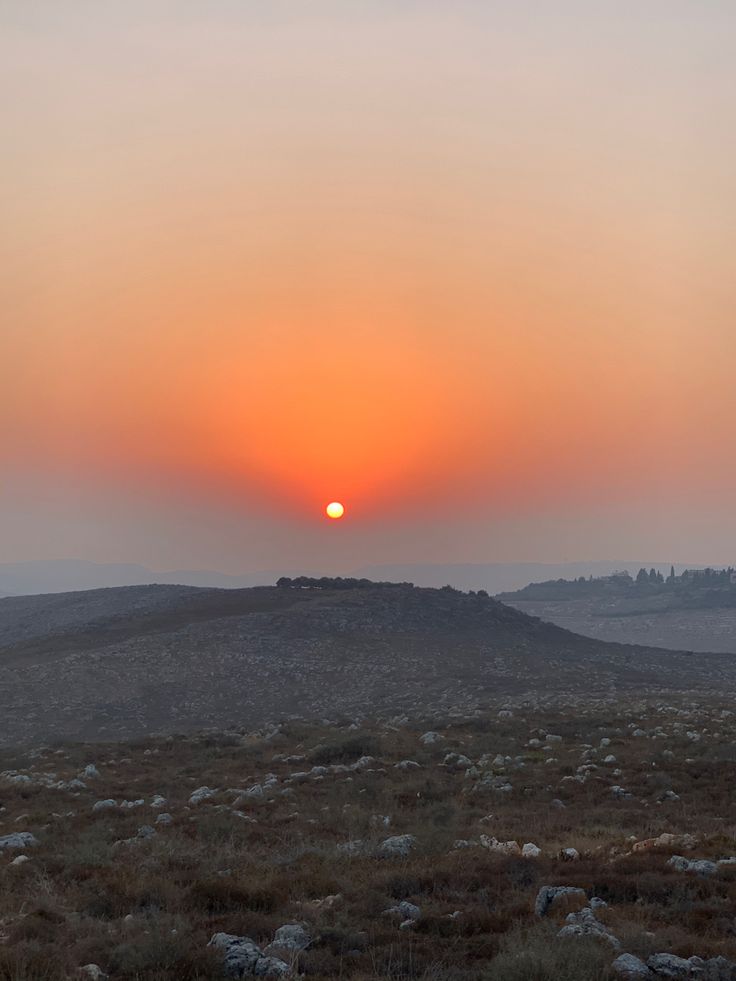 the sun is setting over an open field with rocks and grass in the foreground