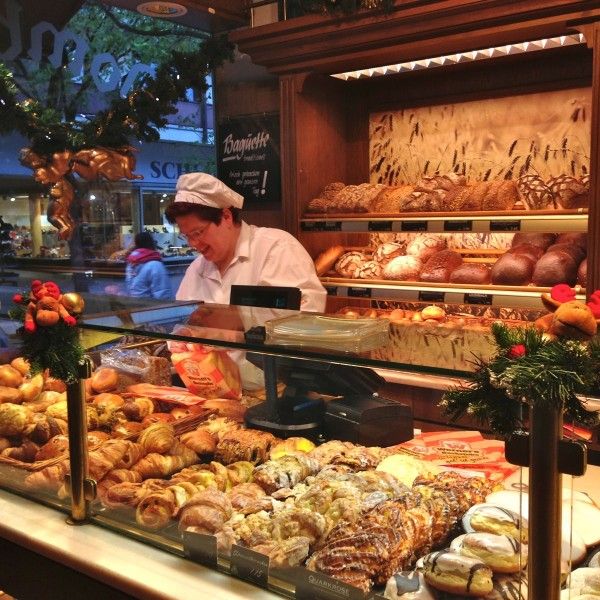 a man working behind the counter of a bakery selling breads and pastries to customers