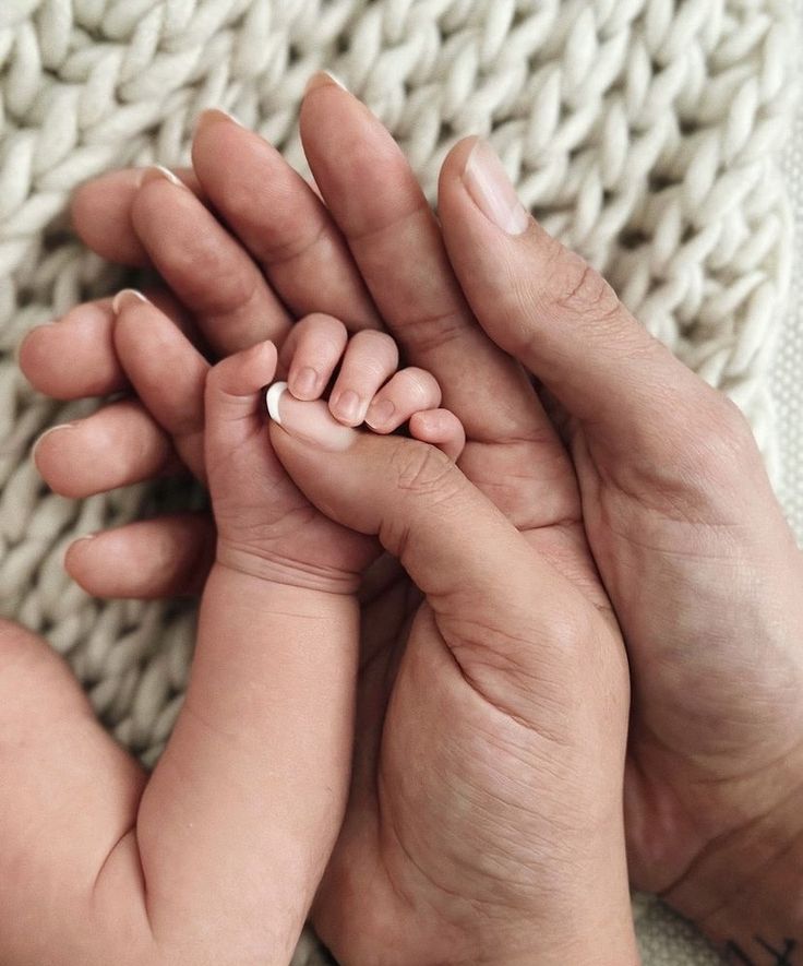 two hands holding a newborn baby's hand