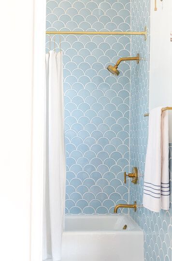 a bathroom with blue and white tiles, gold faucet, shower curtain, and bathtub