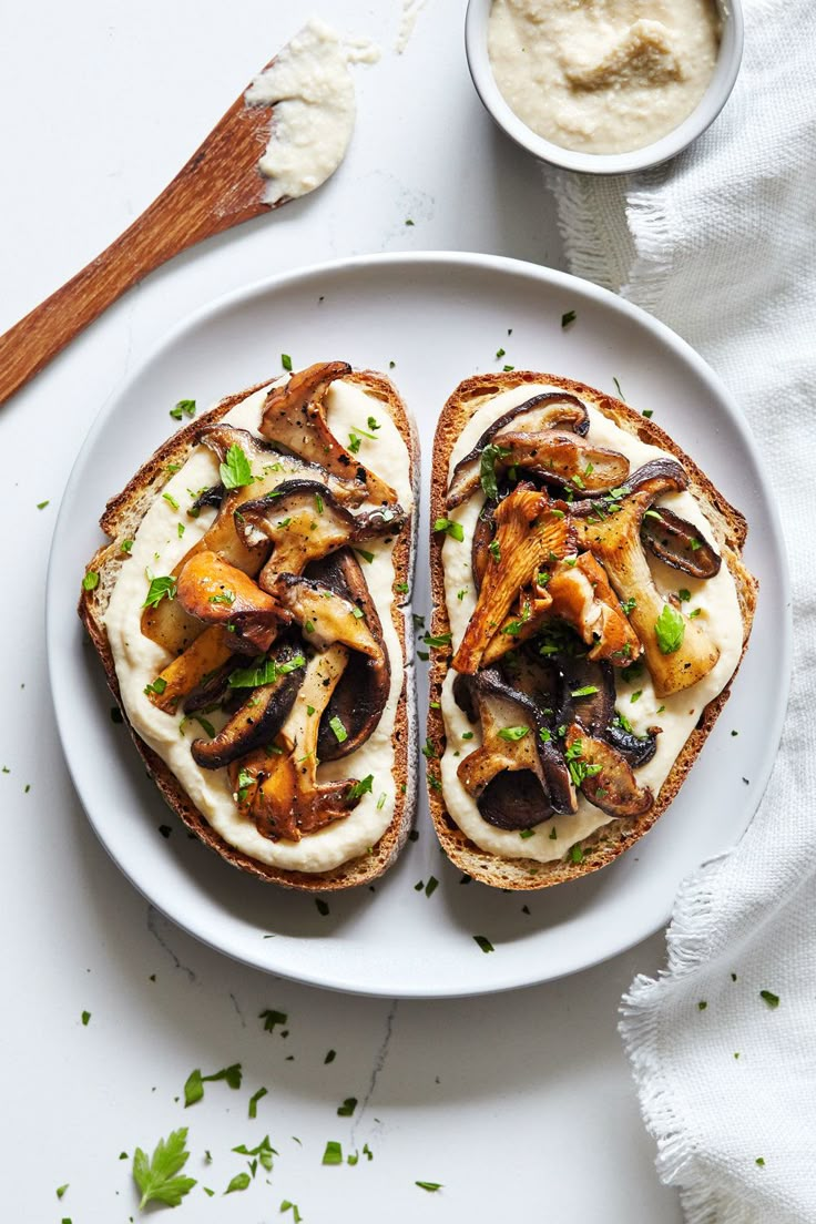 two pieces of bread on a white plate with mushrooms and cream sauce in the background