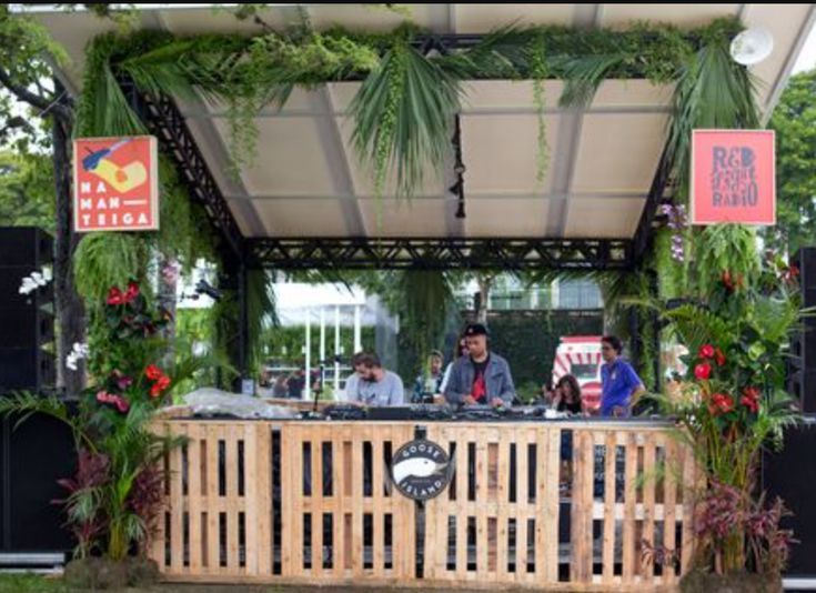 some people are sitting at a wooden bar with plants on it and signs hanging from the roof