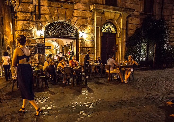 people are sitting at tables outside in the evening