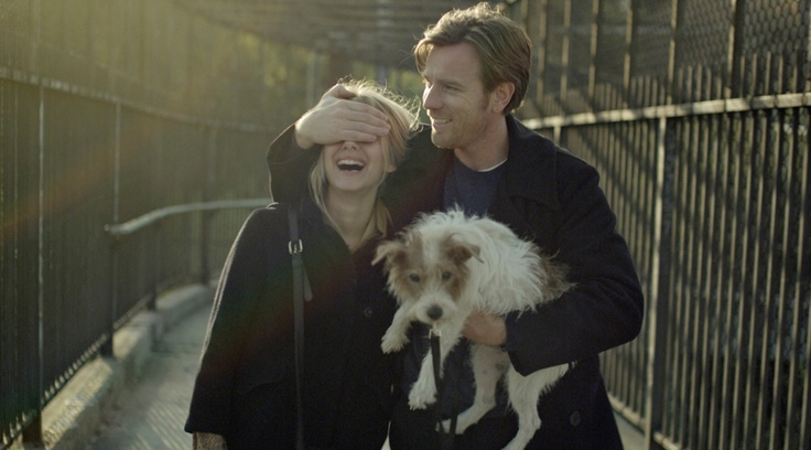 two people walking down a bridge with a dog in their arms and one person smiling