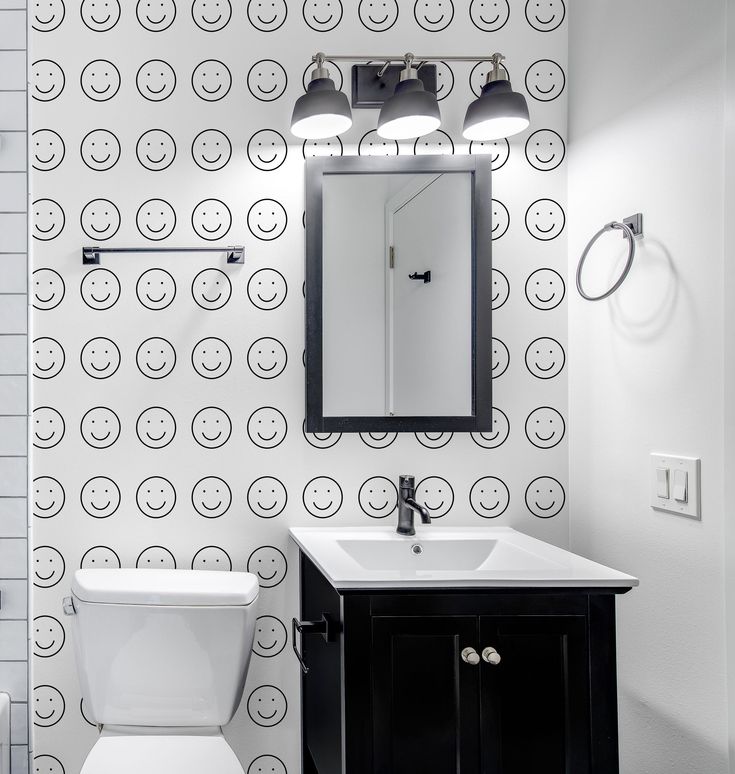 a white toilet sitting under a bathroom mirror next to a sink and a wall mounted faucet