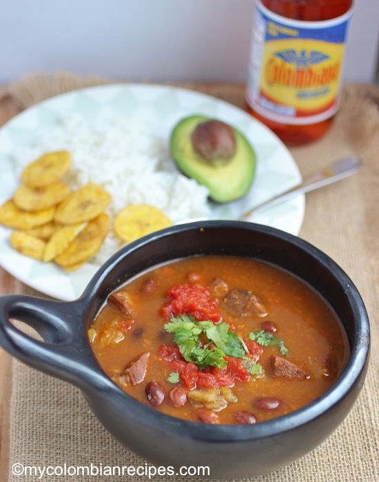 a black bowl filled with soup next to a plate of chips and an avocado