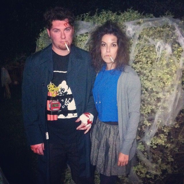 a man and woman standing next to each other in front of a wall with plants growing on it