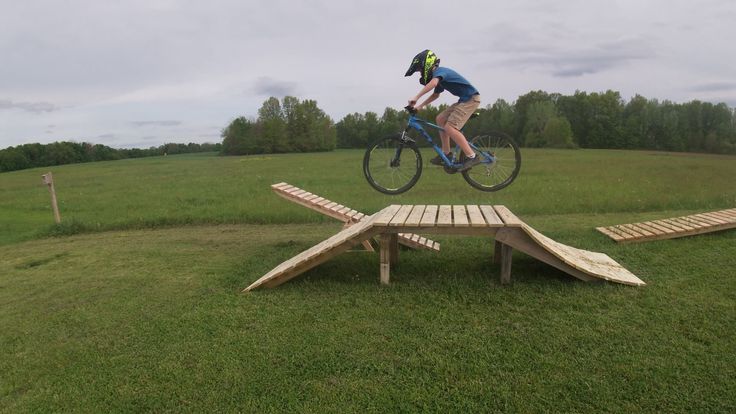 a man riding a bike over a wooden bench on top of a grass covered field