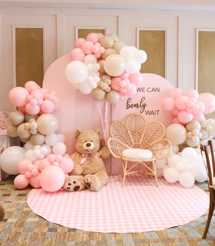 a teddy bear sitting in front of a bunch of balloons on a table next to a chair