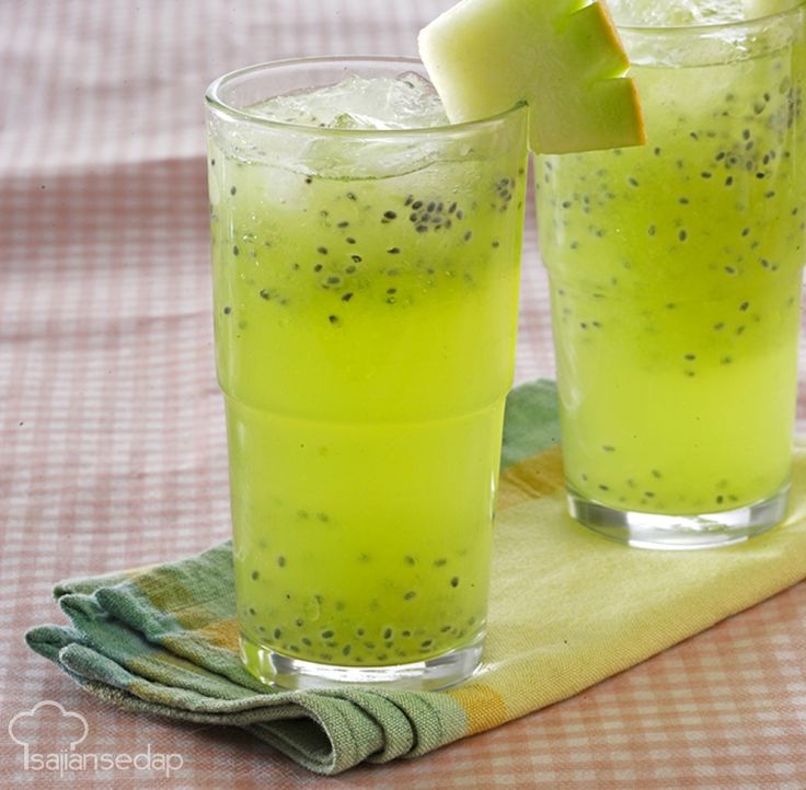 two glasses filled with green liquid sitting on top of a table next to a slice of fruit