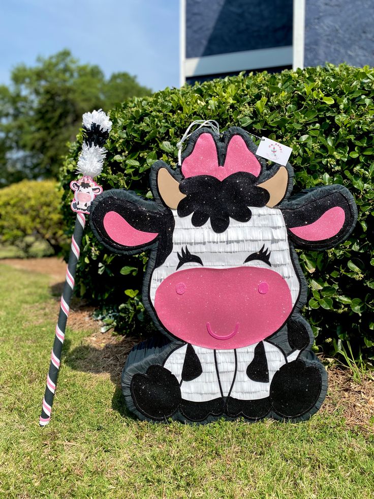 a cow statue sitting in the grass with a candy cane next to it's mouth