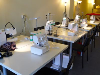 several sewing machines are lined up on the tables in a room with chairs and lamps