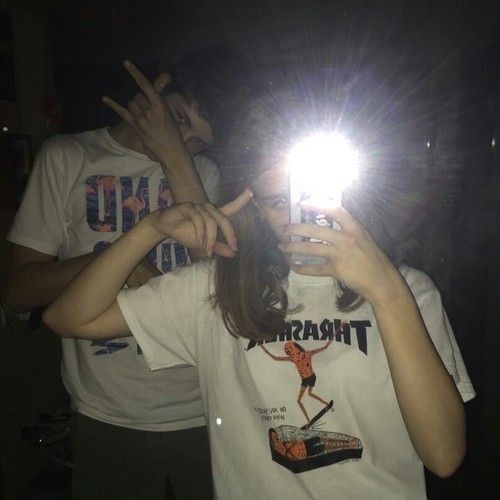 two people standing in front of a mirror taking pictures with their cell phones at night