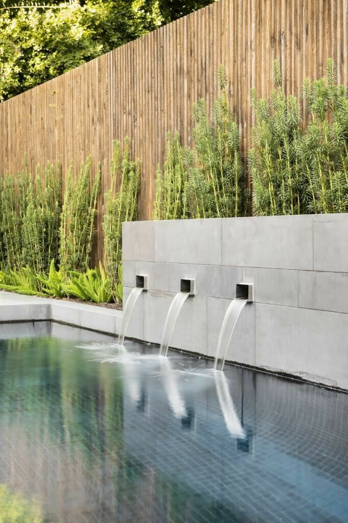 an outdoor pool with water running from it and plants growing on the wall next to it