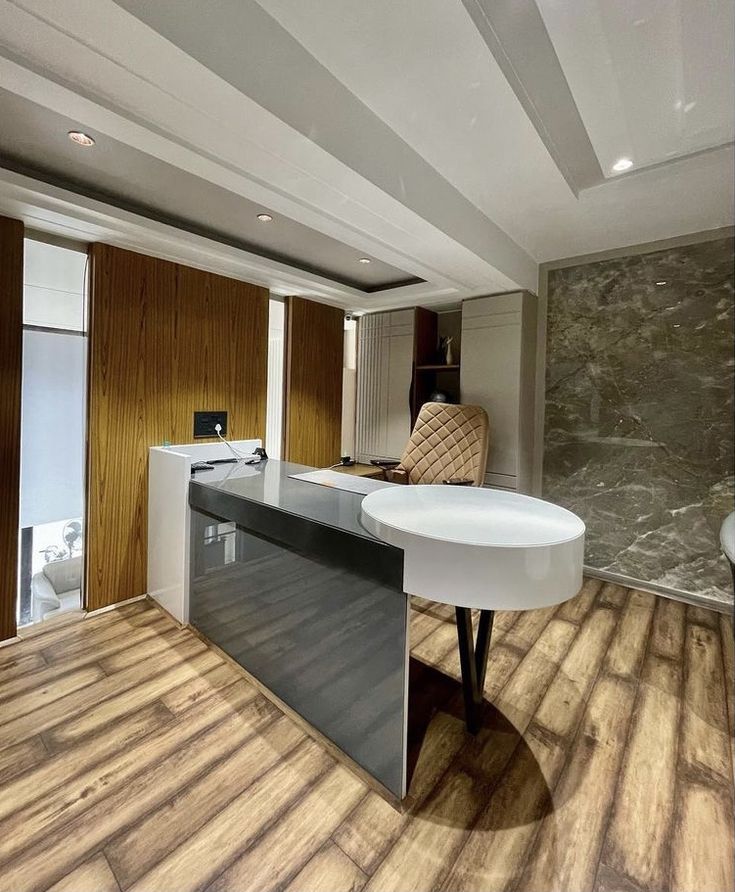 an office with wood flooring and white desk in front of a marble wall behind it