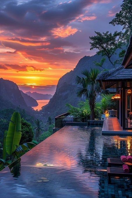 an outdoor pool with mountains in the background at sunset or sunrise, and people sitting on lounge chairs looking out to sea