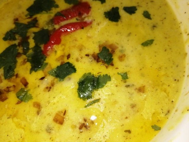 a white bowl filled with yellow soup and garnished with green leafy toppings