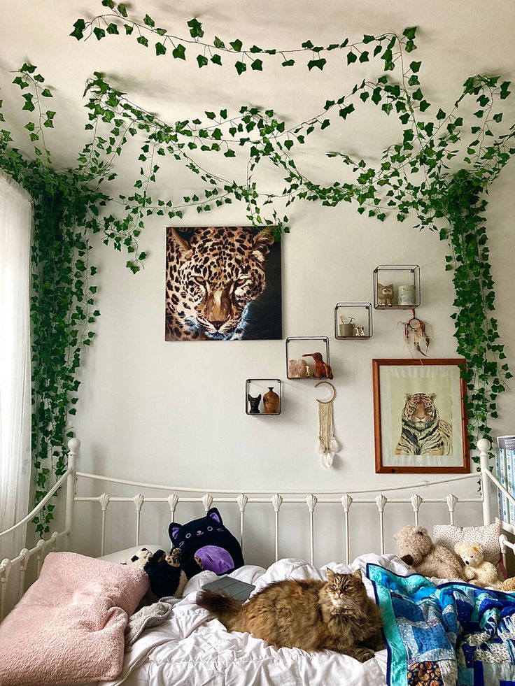 a cat laying on top of a bed under a green vine covered ceiling with pictures above it